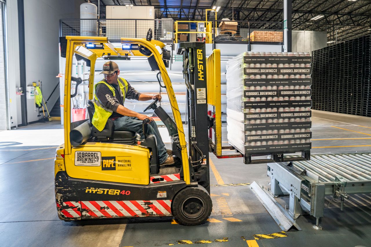 A forklift moving pallets of goods inside a busy warehouse